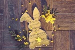 Easter bunny silhouette in music sheet with yellow flowers on wood background.